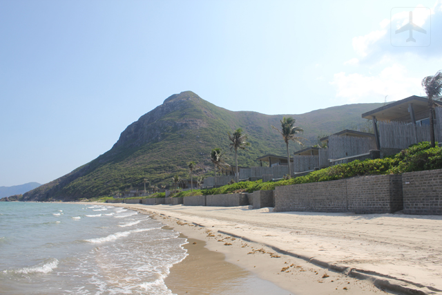 The spacious strip of beach with villas lined at the side.